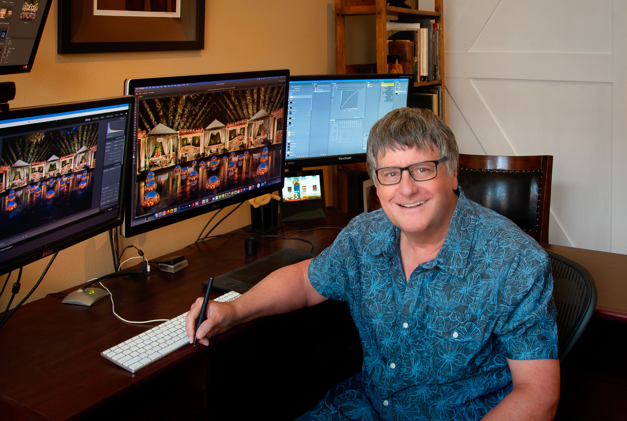 Randy Galligan at his retouching workstation, holding a tablet pen with resort photographs on his monitors.